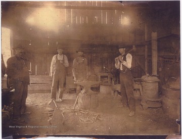 A look at the interior of the old owned by Joseph Neely, who is pictured wearing overalls and a white shirt. Man to the far left with the mustache is John Crush. The man by the stove with a hammer over his shoulder is Abner Wiseman. The fourth man is unidentified. 