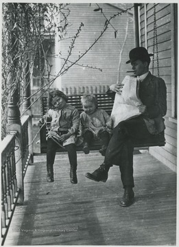A man and his two children relax on the porch swing. Subjects unidentified. 