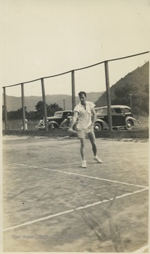 Bill Berry pictured on the court mid-serve. Avis baseball field in the background.