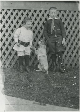 A young boy shakes a dog's paw while standing next to another boy. Subjects unidentified. 