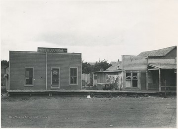 View of the building from across the street. To the right is located a shaving parlor and cleaners.