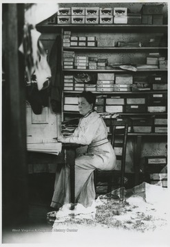 Interior view of the store. An unidentified woman sits at a desk with a newspaper laid out in front of her.