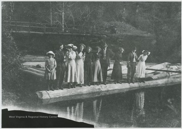 A group of unidentified individuals line themselves on top of a log in the river. 