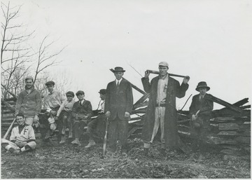 A group poses with baseball bats and gloves by a fence. Subjects unidentified. 