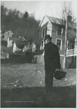 An unidentified man pictures holding a basket near some houses.