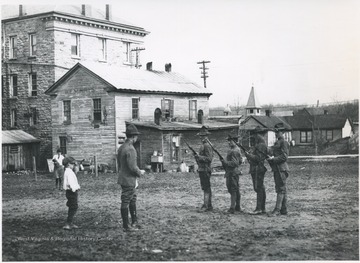 Men in uniform are lined up holding guns while a superior gives instructions. Subjects unidentified. 
