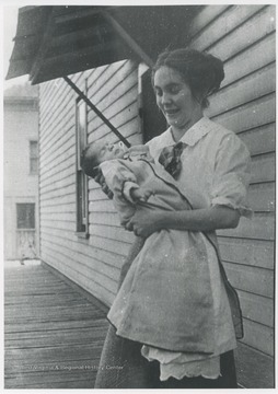 Mrs. White cradles her baby on a porch.