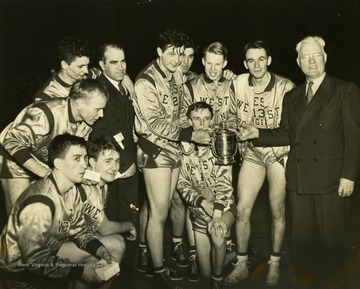 Newspaper clipping on back of photograph reads: "Rudy Baric receives national invitation tournament championship trophy for West Virginia University at Garden last night after Mountaineers, seeded last in field of eight, beat Western Kentucky 47-45, in final. Jack Coffey, Fordham athletic director, makes the presentation. Baric, voted outstanding player of the tournament, is West Virginia's captain and center. Left to right kneeling are: Dick Kesling, Scotty Hamilton and Roger Hicks (behind trophy). Left to right standing are Walter Rollins, Lou Kalmar (with arm around coach's shoulder), Coach Dyke Raese, Baric, Neil Montone, George Rickey, Don Raese and Coffey."
