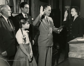 Clerk C.A. Blankenship administers the oath to Helen Holt who succeeded her late husband Rush D. Holt  as Lewis County's representative. Rush Holt died before he could take office. Their daughter, Helen Jane, Mrs. Holt's father, W.E. Froelich, and House Minority Leader Underwood look on.
