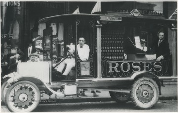 An unidentified man sits behind the wheel of an automobile advertising the store located on Temple Street and 3rd Avenue. 