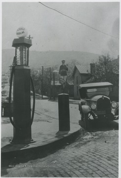 An old-fashioned automobile is parked by a gasoline pump.