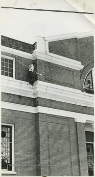 An unidentified man is pictured balancing on a narrow perch toward the roof of the building. 