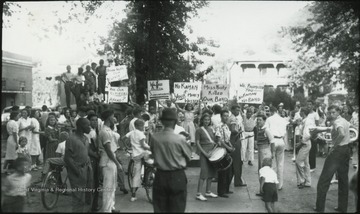 Students holding instruments and signs in protest. One sign reads, "We need a new superintendent". Another reads, "Miss Nicely Killed Our Band". A sign on the top left reads, "Down With Our Female Hitler", and below that sign, "Are Our Citizens Afraid?". Miller Hotel pictured in the background. 