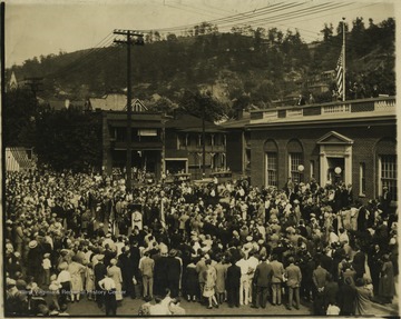 A crowd gathers on the street in front of the building to watch the ceremony. 