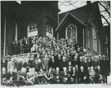A large group of unidentified men, perhaps members of the church, pose along the steps and in front of the building. 