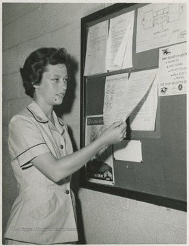 Dick pictured looking at a notice on a board. She was a member of the Women's Army Corps (WAC).