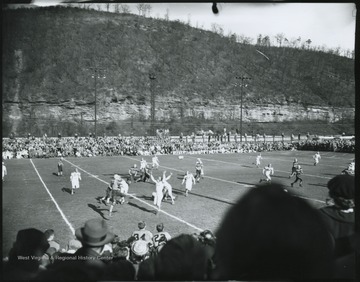 The high school's football team takes on an unidentified opponent. View from the bleachers show spectators lining the field on all sides. 