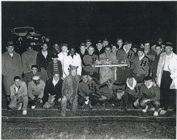 The victorious football team poses with their trophy. The trophy is the Cinderella carriage drawn by horses. Subjects unidentified. 