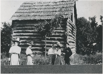 A group of three ladies and two gentleman are pictured beside the log structure. Subjects unidentified. 
