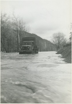 Flood waters surge toward the truck as it attempts to make its way across the road. 