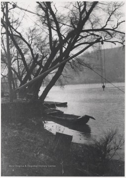 Back of photo reads, "Lower Avis at steamboat dock." A crane hovers over the water where a few canoes gloat nearby. The scene is located in Wyoming County.