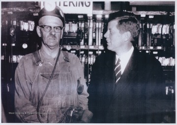 Then senator Kennedy campaigning in the presidential election in 1960 against Richard Nixon. Kennedy's speeches reflected a strong awareness of a significant decline in coal-mining jobs. The coal miner to his left is unidentified. 