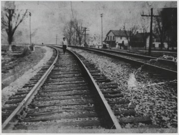 An unidentified man walks along the track. To the left is Lowell hotel. Also to the left is Bill Eades home and O. E. Miller's store. 
