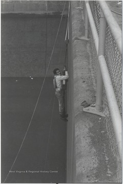Crawford hanging on rope held by pulley system on the side of the dam.