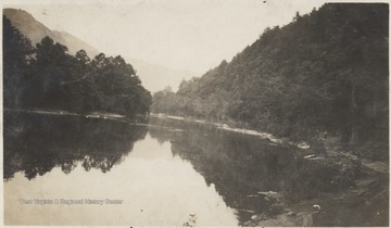 View looking down the river. Two unidentified men are pictured on the far right on top of a rock overlooking the body of water. 