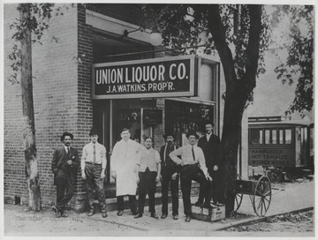 Sign above the bar reads, "Union Liquor Co., J. A. Watkins, proprietor." The store was located on the lower portion of 3rd Avenue. Seven unidentified man pose in front of the entrance.