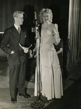 Caption on back of photograph reads: "John Winchcoll, the "Old Timer", and Lois Mae Nolte, singing mistress of ceremonies, have been with the "Musical Steelmakers" series from the start. Winchcoll, an auditor with the company, is a veteran employee, who was chosen as representative of the typical Wheeling employee. Miss Nolte, though only 19, has been on the show in all its seven years, first as one of the Steel Sisters, later as a soloist."