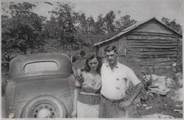 The two Cooks pose next to a car and in front of an old wooden shack.