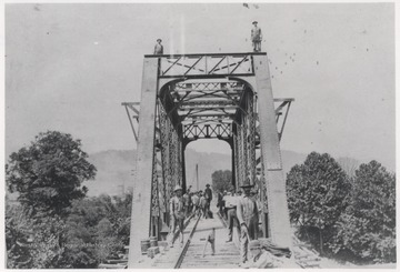 View looking through the line of workers to the other end of the bridge in the town of Lowell. Subjects unidentified.
