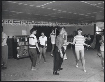 The woman to the right is Dottie Hill. The other unidentified subjects dance with their partners. A jukebox is pictured in the background.