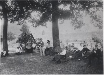 A group of unidentified persons sit out on the boardinghouse's yard. Some play instruments, others lounge on the hammock, and the man to the far right reads. 