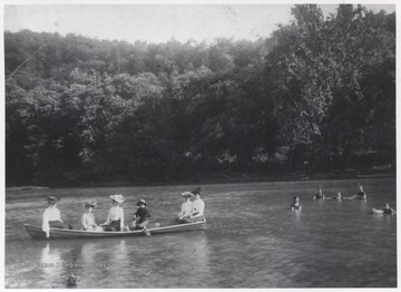A group of women sit inside a canoe while the boys swim beside them. Subjects unidentified.