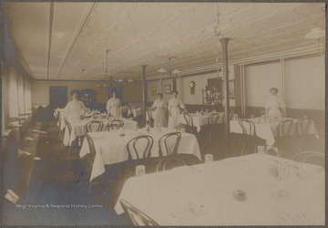Five unidentified women stand beside the neatly set dining tables.