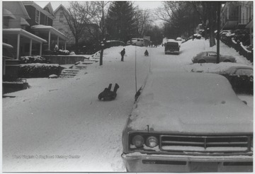An unidentified boy sleds down a snowy hill in a residential neighborhood.