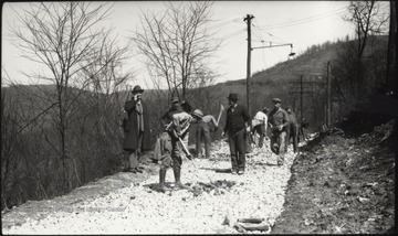 A group of unidentified workers prep the road for paving while a man on the left supervises. 