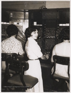 Ms. Farley is pictured beside two unidentified associates in front of the switchboard.