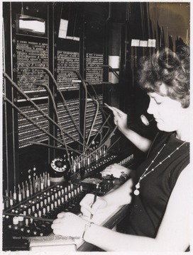 An unidentified woman sits behind the switchboard writing.