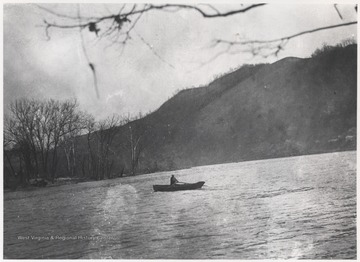 An unidentified man pulls the paddles of his canoe across the river. 
