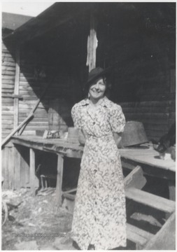 Scott pictured in a sun dress smiling beside a wooden structure.