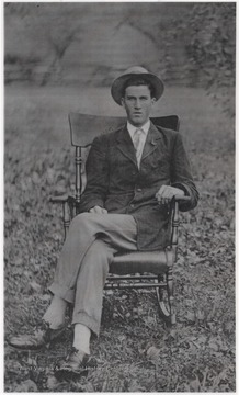Ellison is pictured in fine attire while sitting in a chair positioned in a field.