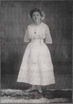 Sheiler poses in a white dress and wears a large bow in her hair.