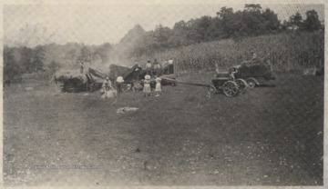 A group of men work on the fields while women observe from the sidelines. 