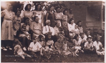 Family members gathered for a family reunion at Alfred Henderson Mann's home. Ezra Lilly is pictured in the center wearing a white shirt and tie. His wife is beside him in the print dress holding a child. 