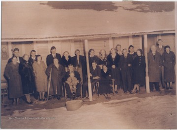 Family members gather to honor the man seated with a child on his lap. Pictured to his left is his son, Oather Jones. Also seated is Mrs. Jones. To the far right is Clarice Roberts who stands in front of Charles Wood and beside a mine superintendent (wearing overcoat). To the far left is Mamie Spurlock, who is standing in front of a member of the Moonlight Strollers Band. 