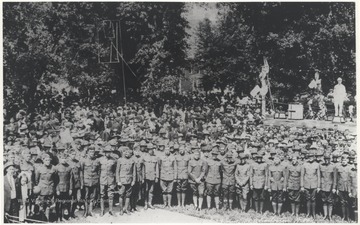 A large group of World War I veterans are pictured outside the park and in front of a stage where musicians are playing instruments. Subjects unidentified. 