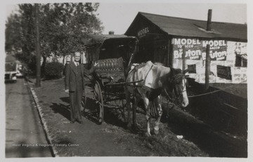 An unidentified man stands beside the carriage just outside the Model Tobacco building. 